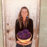Woman holding a bowl of lilac flowers against a rustic wooden door.