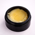 Black container with yellowish substance (Neat Lips: Moisturizing Salve) on a white background