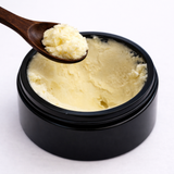 Black container of yellow cream with a wooden spoon on a white background